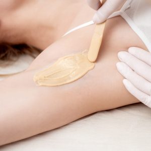 Depilation and epilation female armpit with liquid sugar paste by spatula. Hand of cosmetologist applying wax paste on armpit. Smooth underarm concept